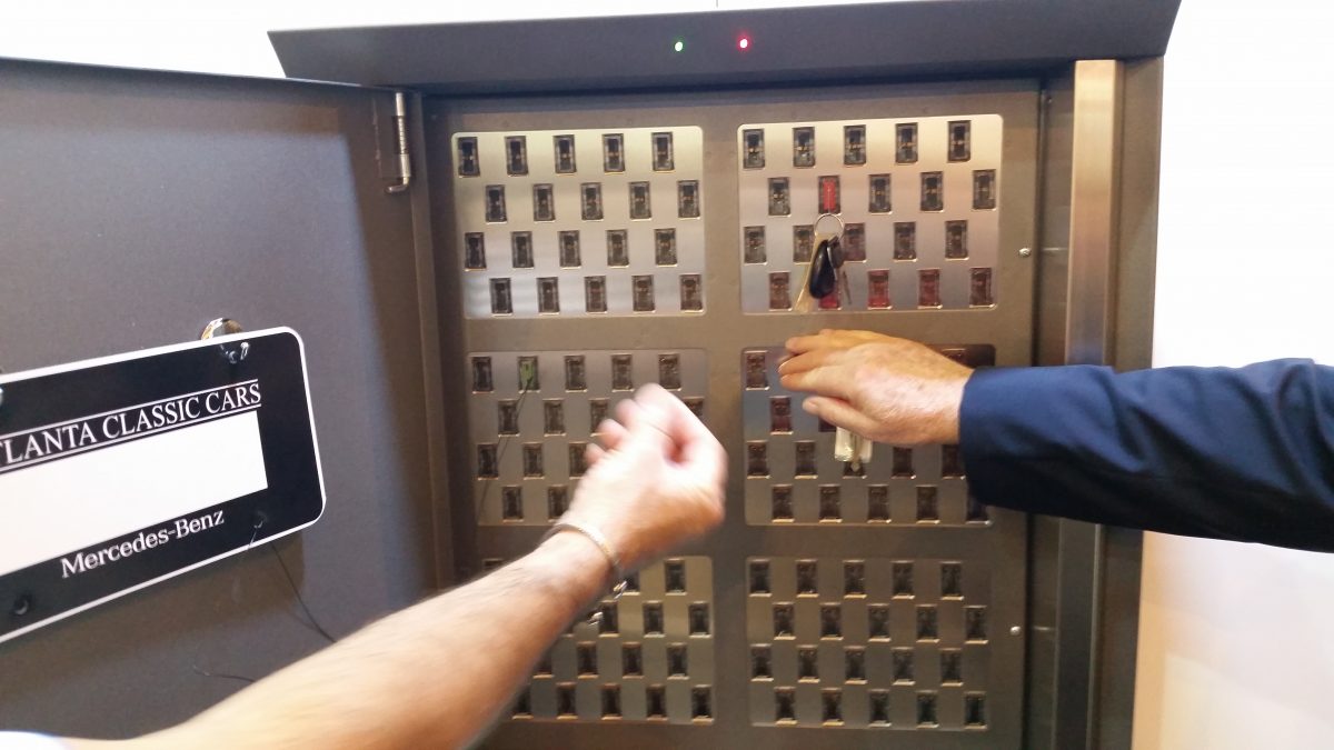 Automotive key management system technology can vary. Image of two hands reaching for keys in a computerized key box.